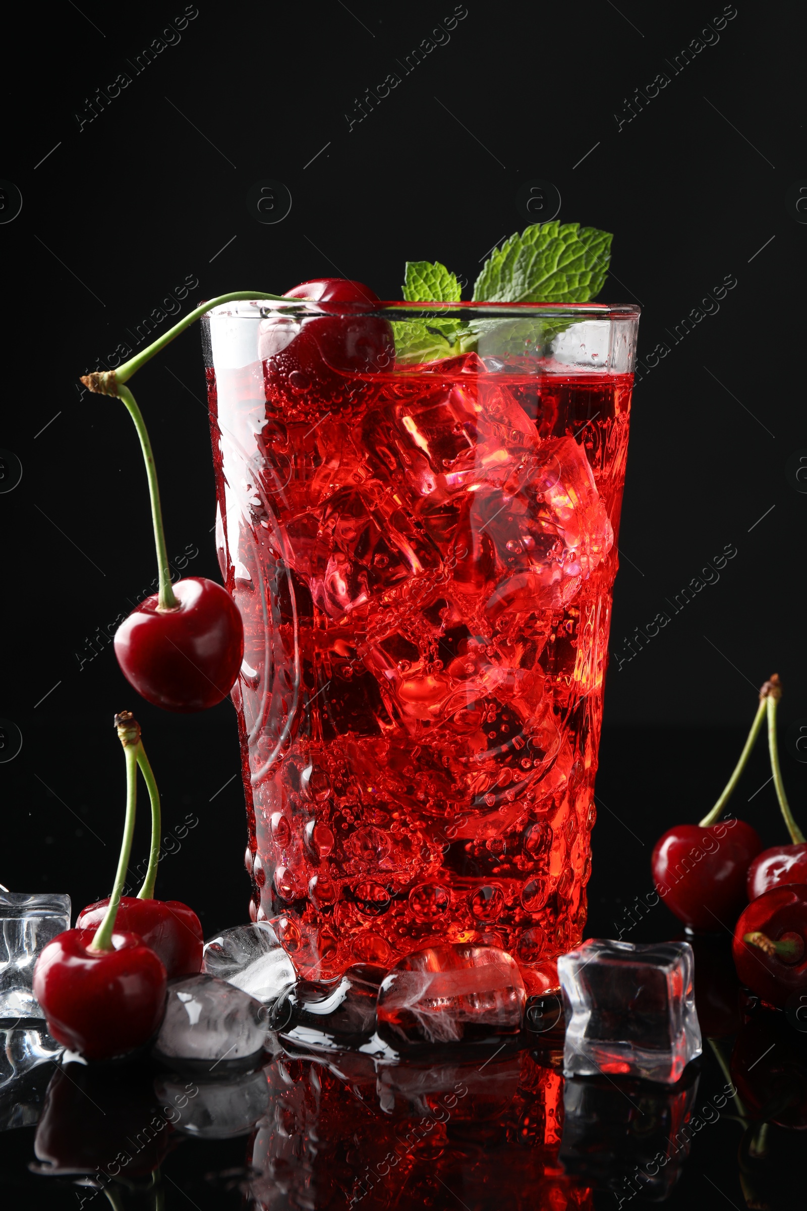Tasty cherry soda with ice cubes, berries and mint in glass on black background, closeup Photo of Tasty cherry soda with ice cubes, berries and mint in glass on black background, closeup