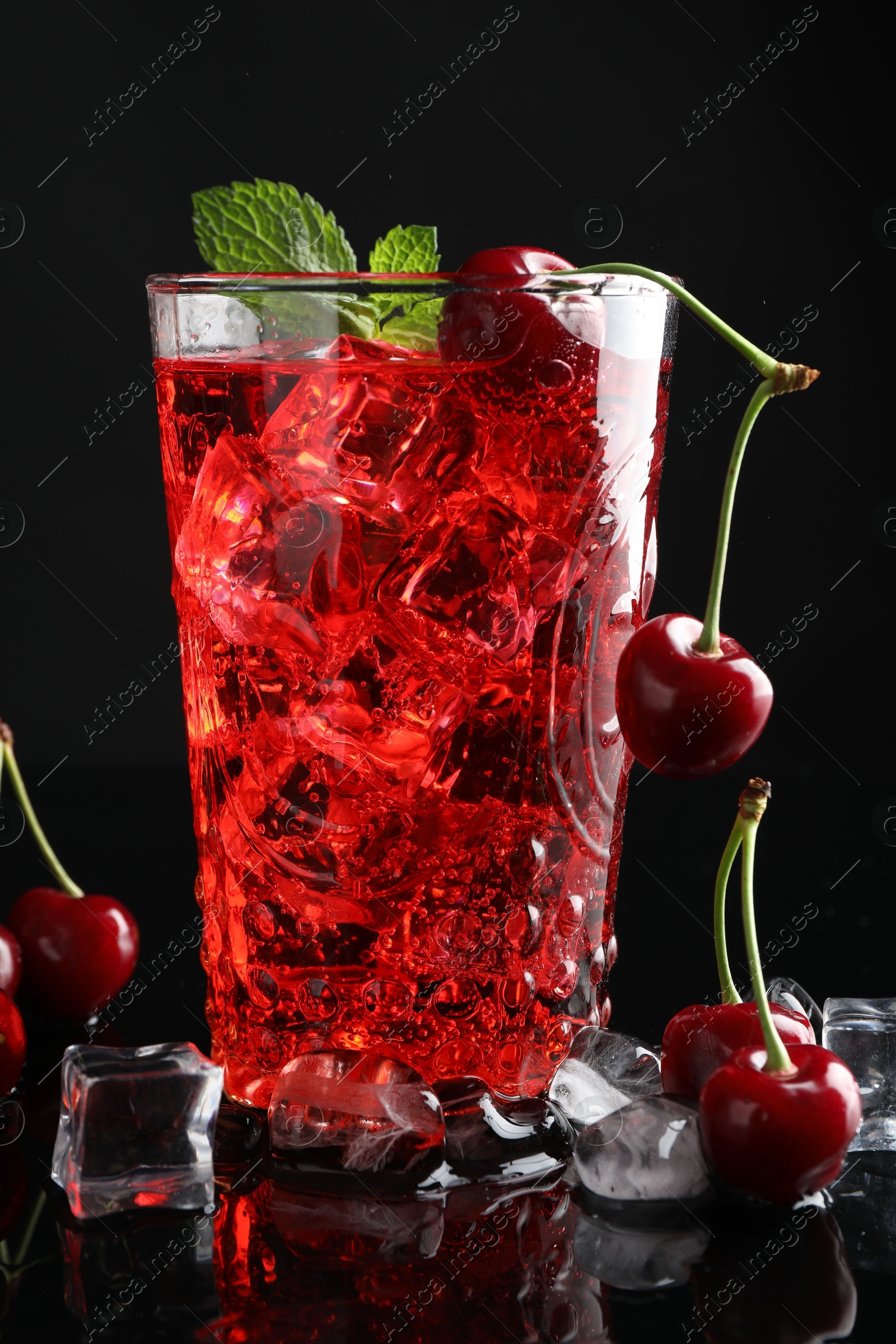 Tasty cherry soda with ice cubes, berries and mint in glass on black background, closeup Photo of Tasty cherry soda with ice cubes, berries and mint in glass on black background, closeup