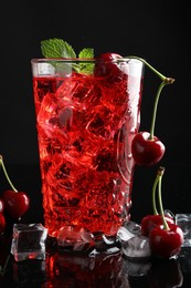 Photo of Tasty cherry soda with ice cubes, berries and mint in glass on black background, closeup