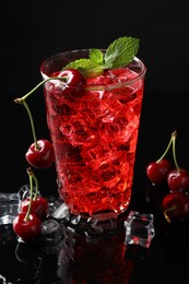 Photo of Tasty cherry soda with ice cubes, berries and mint in glass on black background, closeup