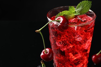 Photo of Tasty cherry soda with ice cubes, berries and mint in glass on black background, closeup. Space for text