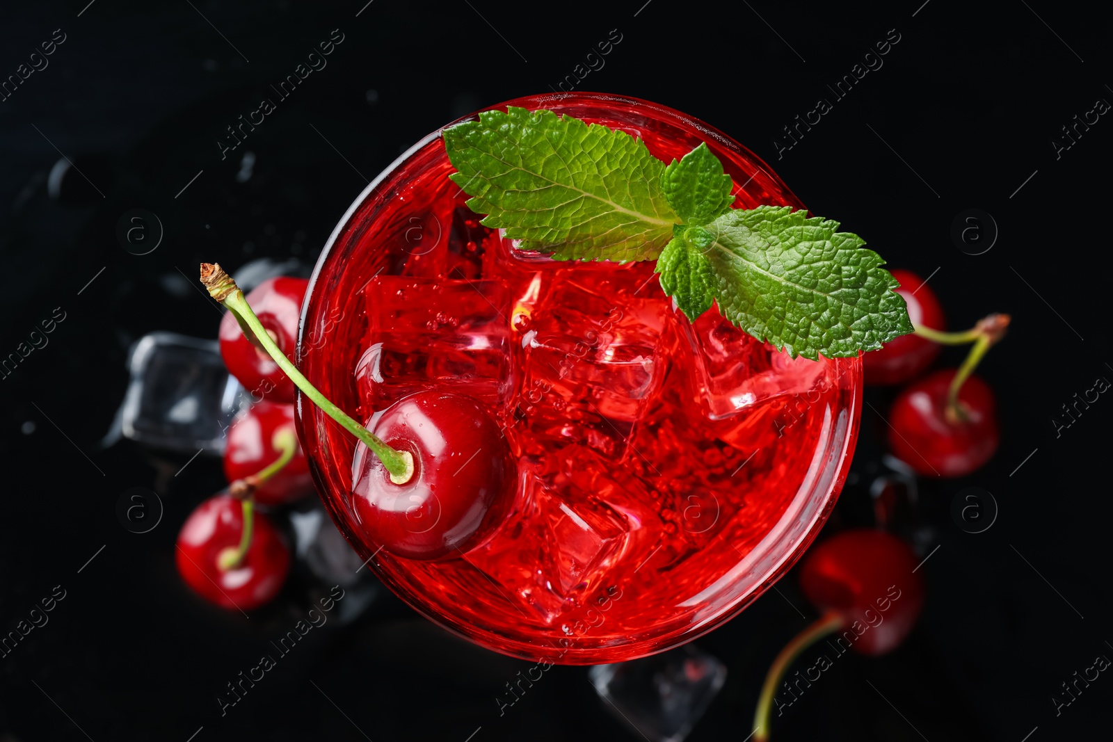 Tasty cherry soda with ice cubes, berries and mint in glass on black background, top view Photo of Tasty cherry soda with ice cubes, berries and mint in glass on black background, top view