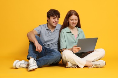 Photo of Teenage girl and boy with laptop on yellow background
