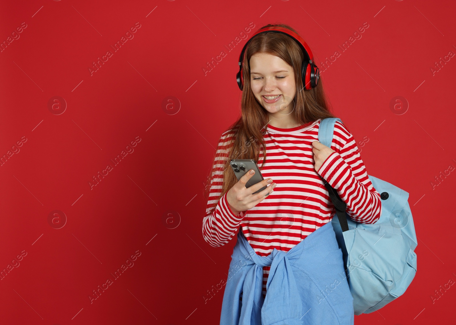 Teenage girl with smartphone listening to music on red background. Space for text Photo of Teenage girl with smartphone listening to music on red background. Space for text