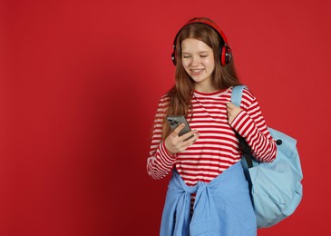 Photo of Teenage girl with smartphone listening to music on red background. Space for text