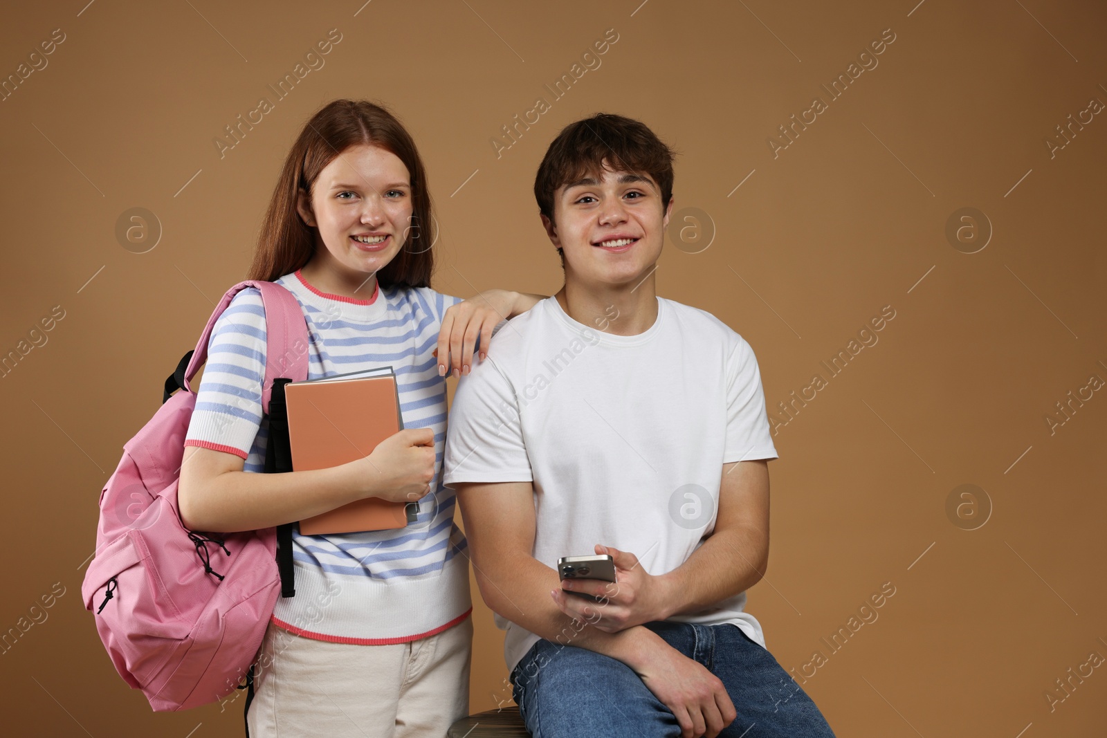 Teenagers with backpack, books and smartphone on brown background Photo of Teenagers with backpack, books and smartphone on brown background