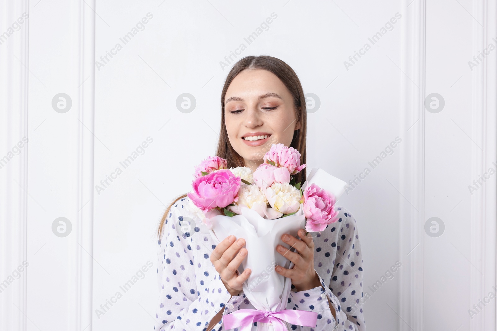 Woman with beautiful bouquet of peonies near white wall indoors Photo of Woman with beautiful bouquet of peonies near white wall indoors