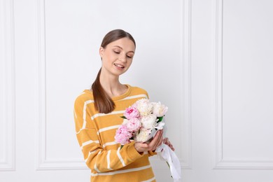 Photo of Woman with beautiful bouquet of peonies near white wall indoors