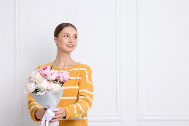 Photo of Woman with beautiful bouquet of peonies near white wall indoors, space for text