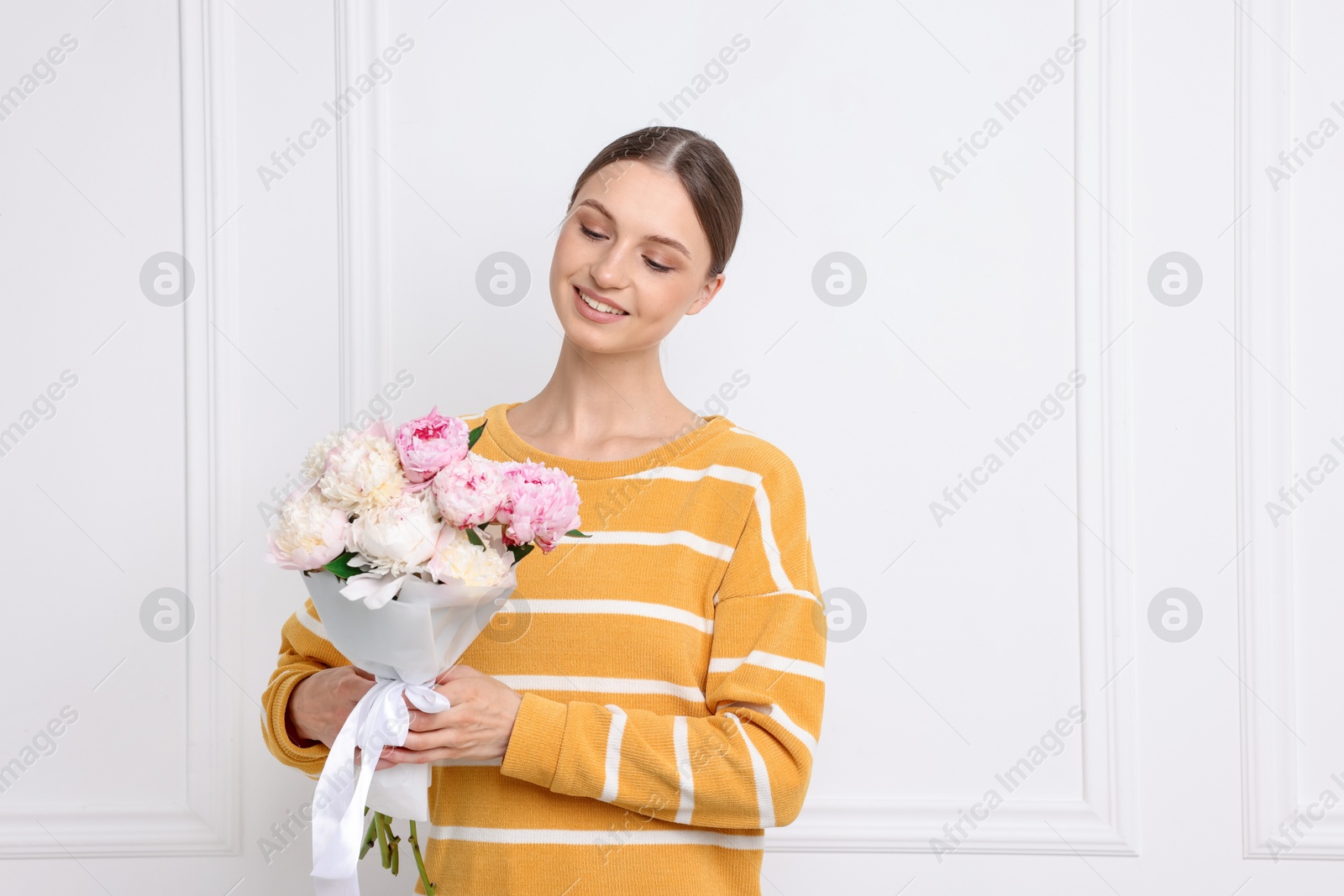 Woman with beautiful bouquet of peonies near white wall indoors Photo of Woman with beautiful bouquet of peonies near white wall indoors