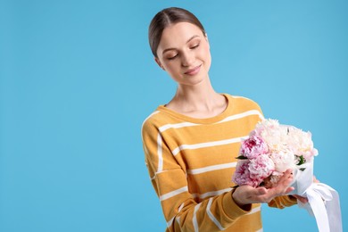 Photo of Woman with beautiful bouquet of peonies on light blue background, space for text