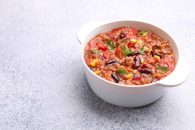 Photo of Tasty chili con carne in bowl on grey table, closeup. Space for text