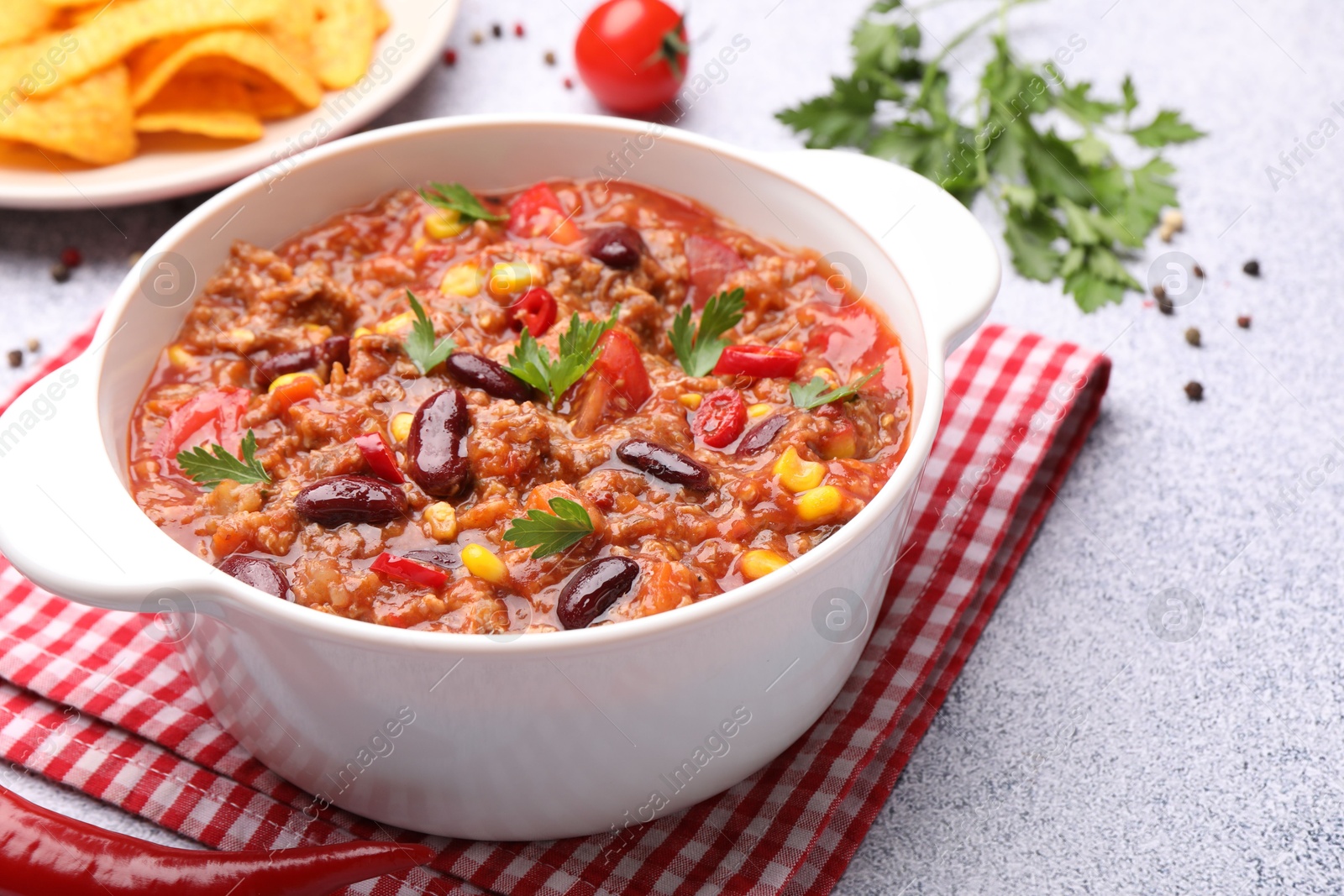 Tasty chili con carne in bowl, nachos and ingredients on grey table, closeup Photo of Tasty chili con carne in bowl, nachos and ingredients on grey table, closeup