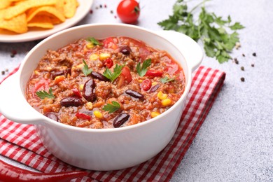 Photo of Tasty chili con carne in bowl, nachos and ingredients on grey table, closeup