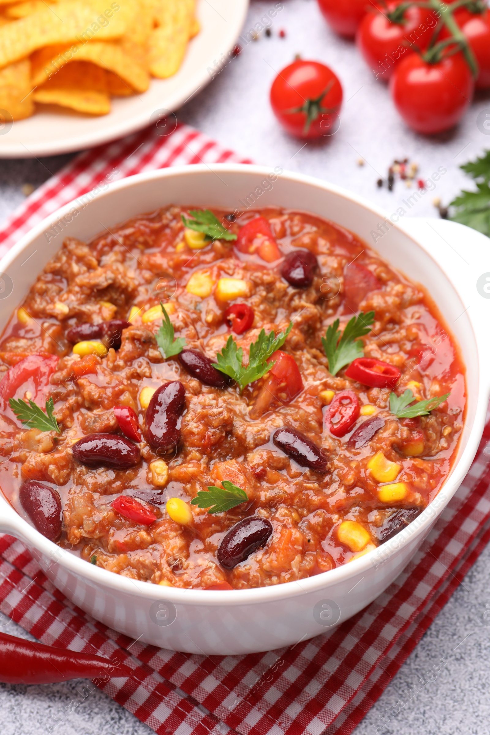 Tasty chili con carne in bowl, nachos and ingredients on grey table, closeup Photo of Tasty chili con carne in bowl, nachos and ingredients on grey table, closeup