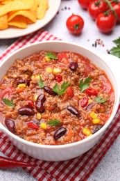Photo of Tasty chili con carne in bowl, nachos and ingredients on grey table, closeup