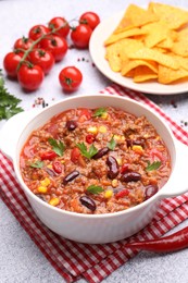 Photo of Tasty chili con carne in bowl, nachos and ingredients on grey table, closeup