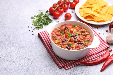 Photo of Tasty chili con carne in bowl, nachos and ingredients on grey table, closeup. Space for text