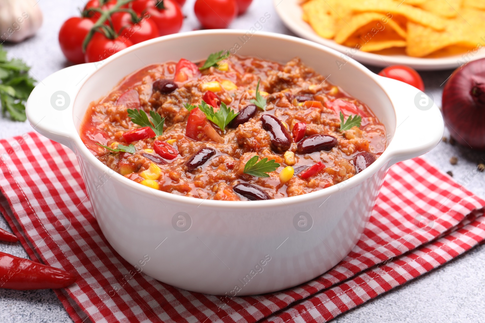 Tasty chili con carne in bowl, nachos and ingredients on grey table, closeup Photo of Tasty chili con carne in bowl, nachos and ingredients on grey table, closeup
