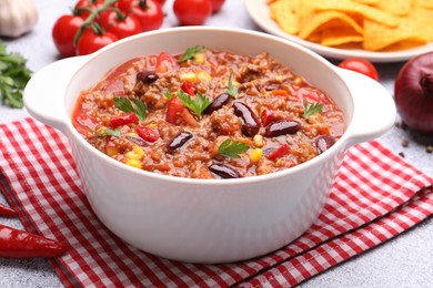 Photo of Tasty chili con carne in bowl, nachos and ingredients on grey table, closeup