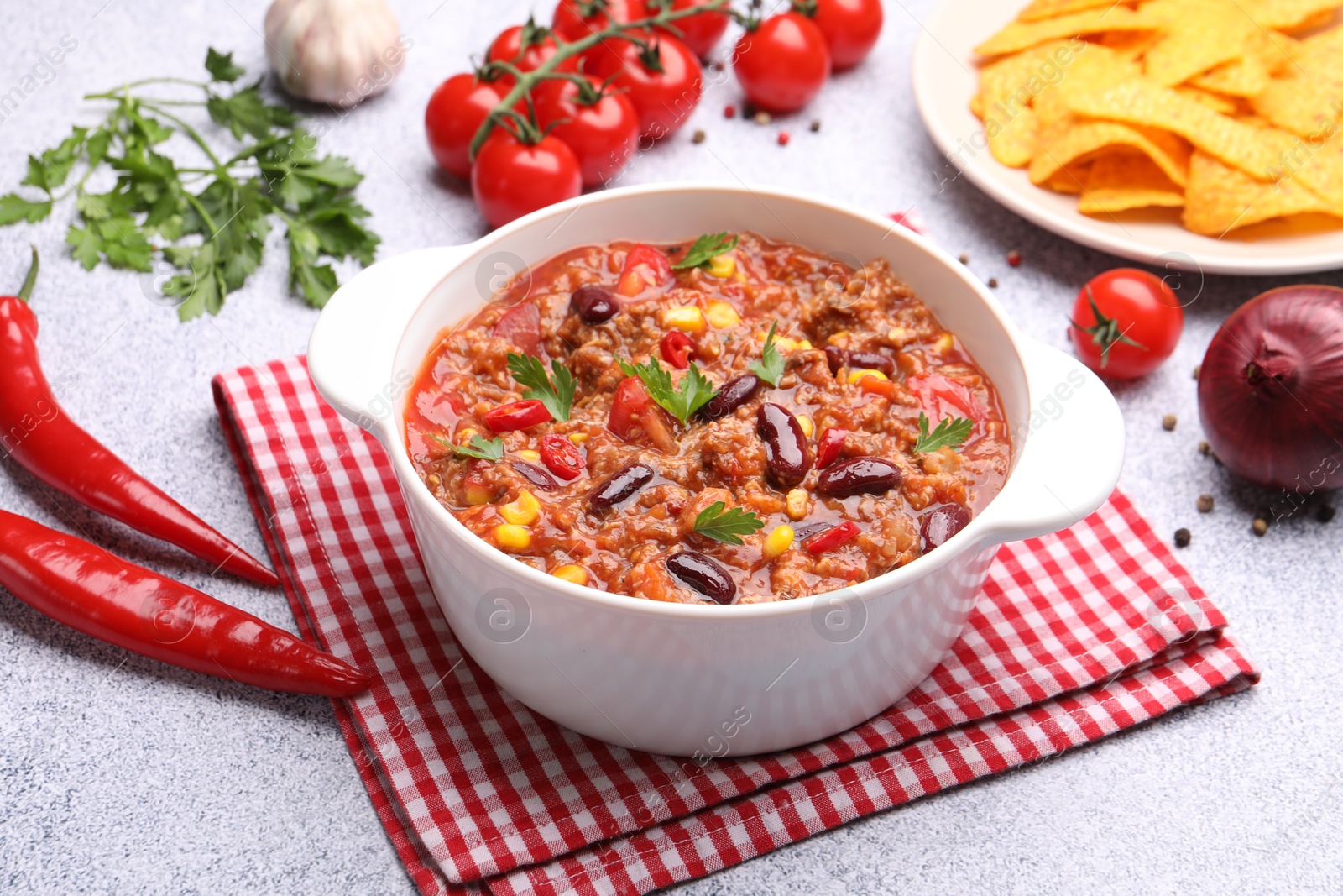 Tasty chili con carne in bowl, nachos and ingredients on grey table, closeup Photo of Tasty chili con carne in bowl, nachos and ingredients on grey table, closeup