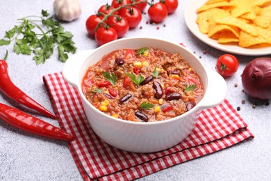 Photo of Tasty chili con carne in bowl, nachos and ingredients on grey table, closeup