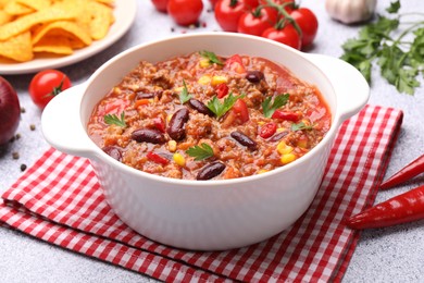 Photo of Tasty chili con carne in bowl, nachos and ingredients on grey table, closeup