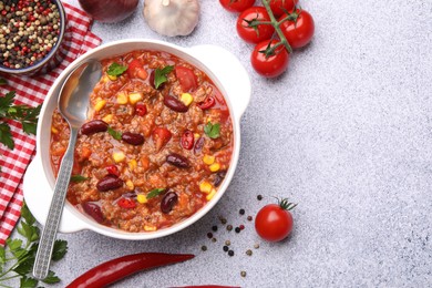 Photo of Tasty chili con carne in bowl and ingredients on grey table, flat lay. Space for text