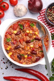 Photo of Tasty chili con carne in bowl and ingredients on grey table, flat lay