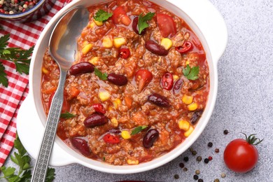 Photo of Tasty chili con carne in bowl and ingredients on grey table, flat lay