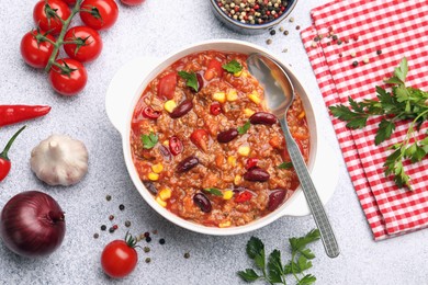 Photo of Tasty chili con carne in bowl and ingredients on grey table, flat lay