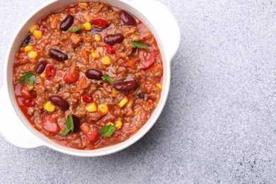 Photo of Tasty chili con carne in bowl on grey table, top view. Space for text