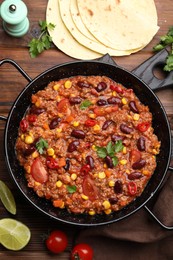 Photo of Tasty chili con carne in baking dish and flatbread on wooden table, flat lay