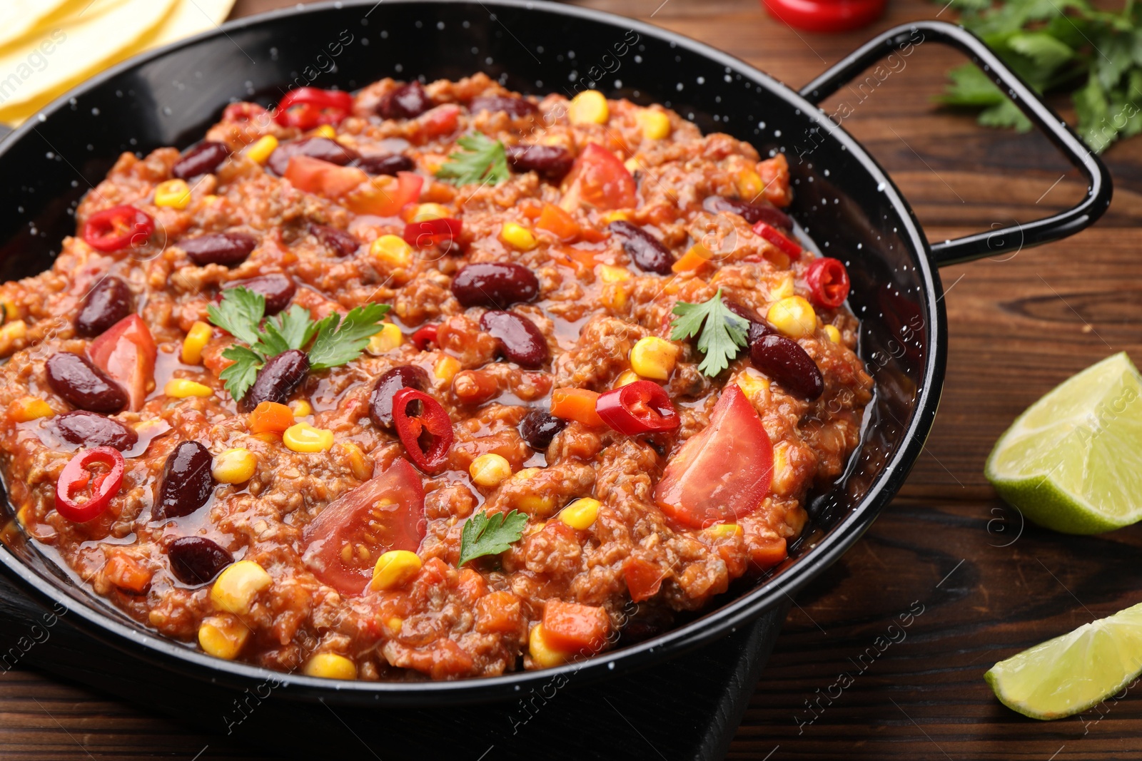 Photo of Tasty chili con carne in baking dish on wooden table, closeup