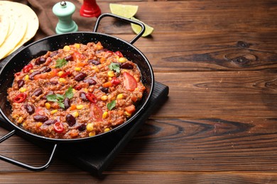 Photo of Tasty chili con carne in baking dish and flatbread on wooden table, closeup. Space for text