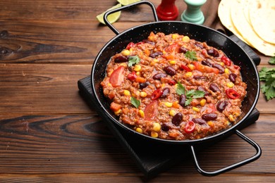 Photo of Tasty chili con carne in baking dish and flatbread on wooden table, closeup. Space for text