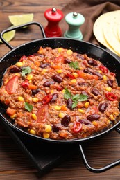 Photo of Tasty chili con carne in baking dish on wooden table, closeup