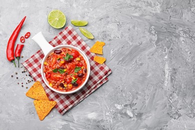 Photo of Tasty chili con carne in bowl and nachos on grey textured table, flat lay. Space for text