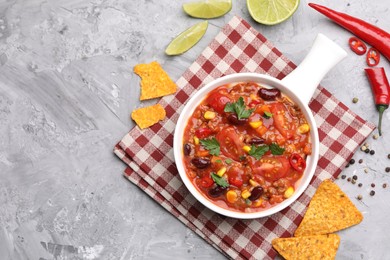 Photo of Tasty chili con carne in bowl and nachos on grey textured table, flat lay. Space for text