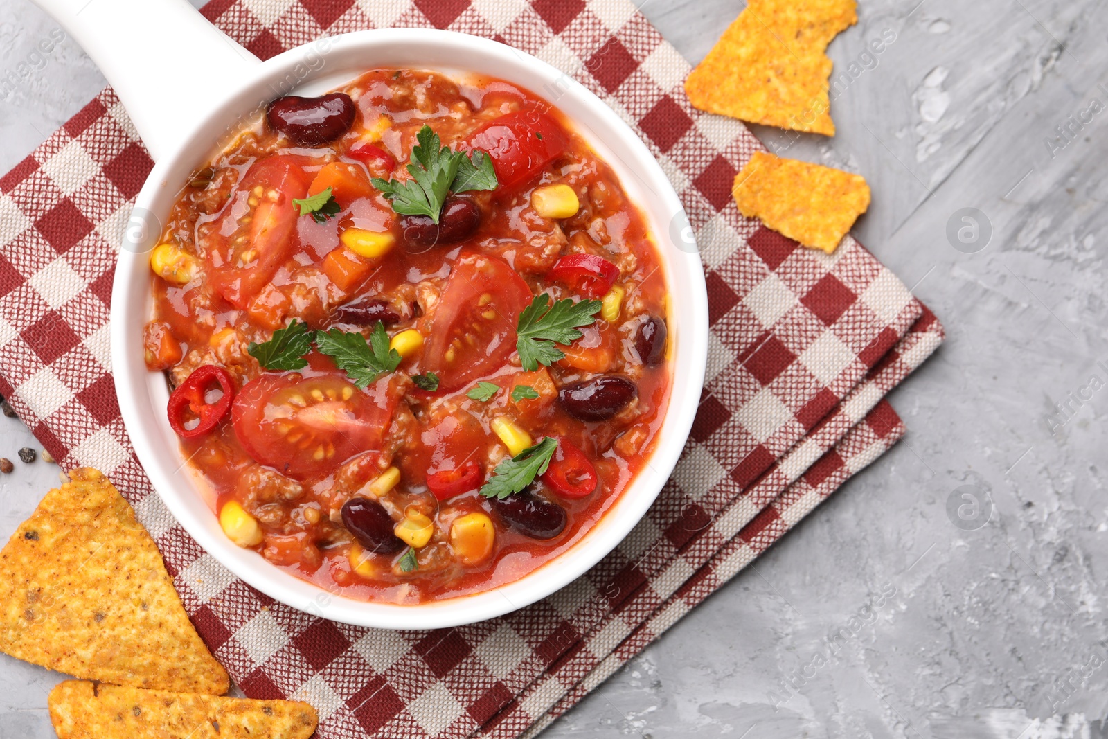 Tasty chili con carne in bowl and nachos on grey textured table, flat lay Photo of Tasty chili con carne in bowl and nachos on grey textured table, flat lay