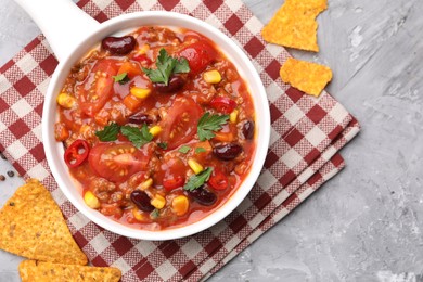 Photo of Tasty chili con carne in bowl and nachos on grey textured table, flat lay