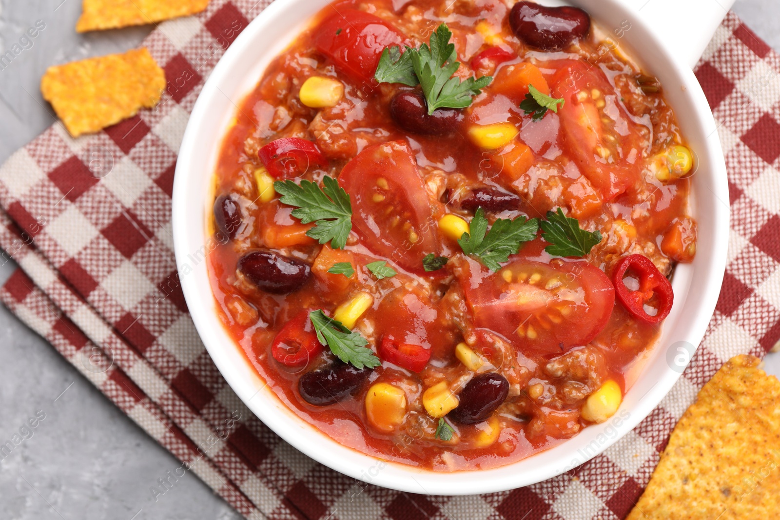 Tasty chili con carne in bowl and nachos on grey textured table, flat lay Photo of Tasty chili con carne in bowl and nachos on grey textured table, flat lay