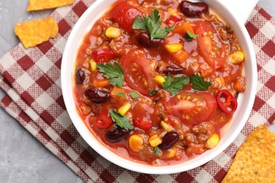 Photo of Tasty chili con carne in bowl and nachos on grey textured table, flat lay