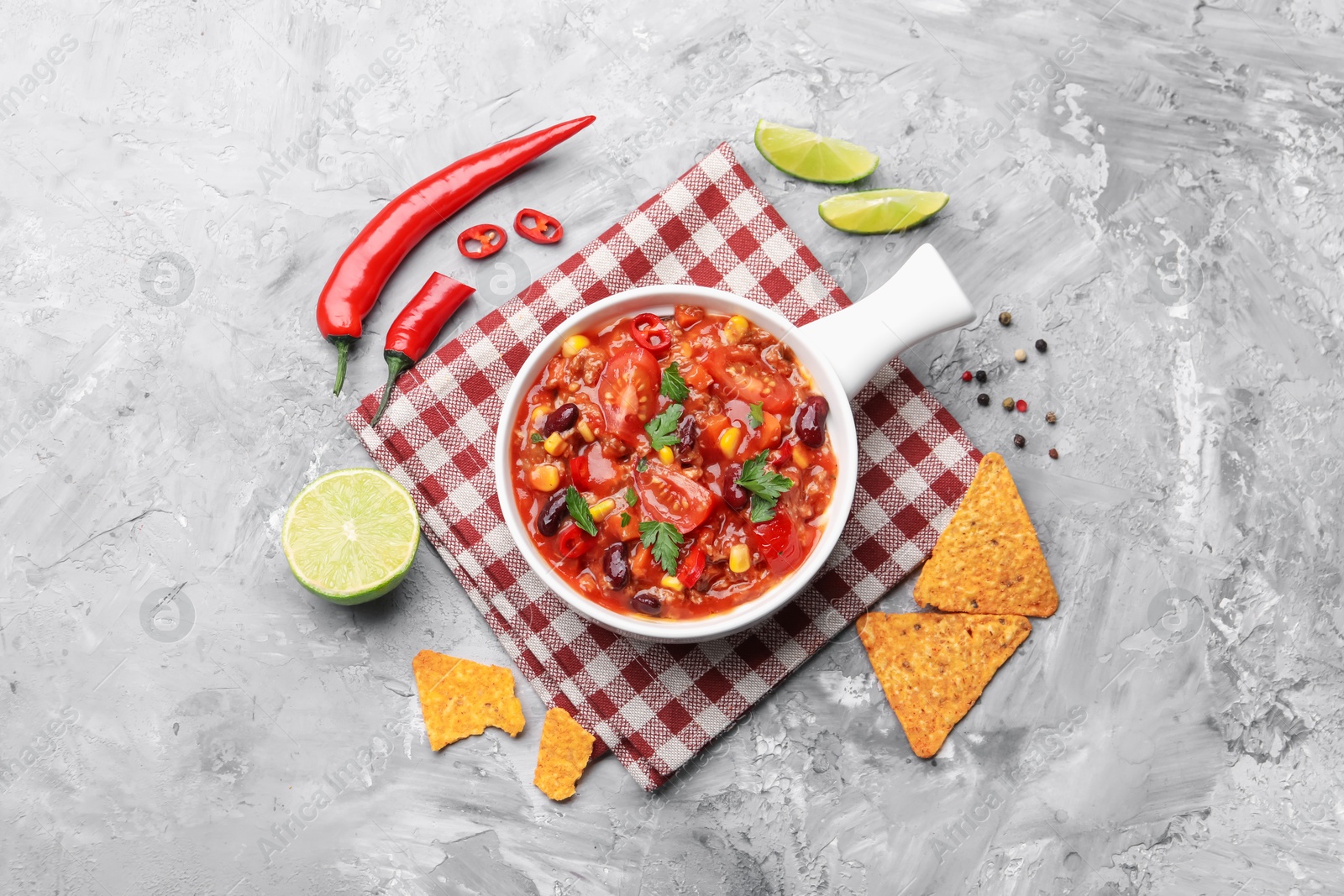 Tasty chili con carne in bowl and nachos on grey textured table, flat lay Photo of Tasty chili con carne in bowl and nachos on grey textured table, flat lay