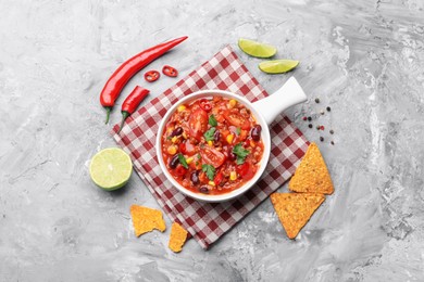 Photo of Tasty chili con carne in bowl and nachos on grey textured table, flat lay
