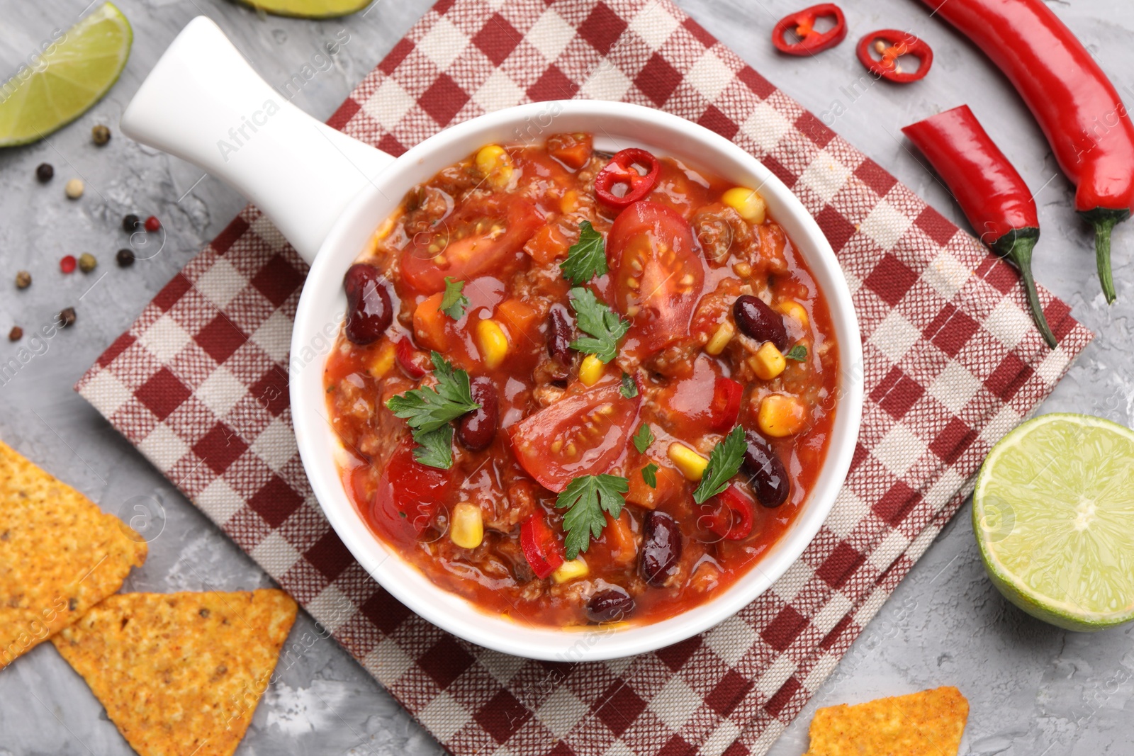 Tasty chili con carne in bowl and nachos on grey textured table, flat lay Photo of Tasty chili con carne in bowl and nachos on grey textured table, flat lay