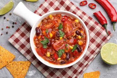 Photo of Tasty chili con carne in bowl and nachos on grey textured table, flat lay