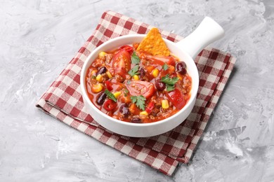 Photo of Tasty chili con carne in bowl and nachos on grey textured table, closeup