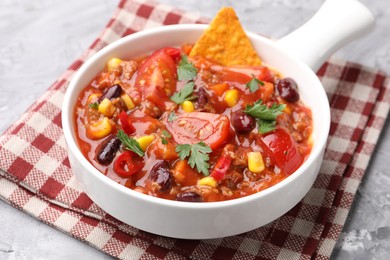 Photo of Tasty chili con carne in bowl and nachos on grey textured table, closeup