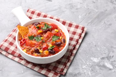 Photo of Tasty chili con carne in bowl and nachos on grey textured table, closeup. Space for text